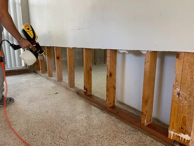 Force1 Restoration technician applying EPA-registered antimicrobial treatment to exposed wall studs during water damage mold prevention protocol